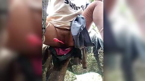 Media: Video of a young woman, possibly of mixed ethnicity, partially undressed in a wooded area. She wears a beige shirt and pink panties. Her exposed buttocks and legs are visible.