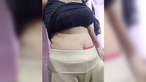 Media: Video of a woman lifting her black top to reveal a red bra, wearing beige pants, in a dimly lit room with purple walls.