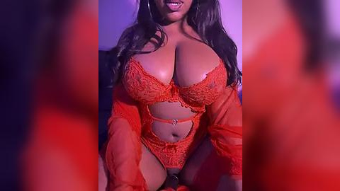 Media: Video of a voluptuous, dark-skinned woman with large breasts, wearing an intricate, orange lace lingerie set, with long, wavy hair, and a playful expression. The background is dimly lit with purple and red hues.