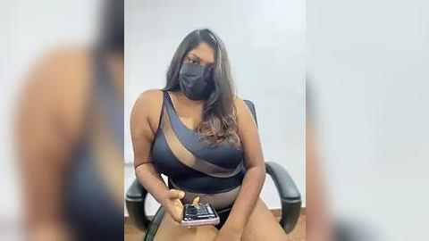 Media: Video of a dark-skinned woman with long black hair, wearing a black mask and revealing black lingerie, seated at a desk, holding a cigarette.