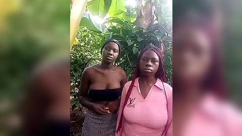 Media: Video of two African women with dark skin, one in a black bandeau top and gray skirt, the other in a pink polo shirt. They stand in a lush, green tropical garden, surrounded by banana leaves and foliage.