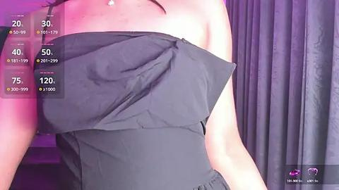 Media: Video of a woman wearing a strapless black dress with a ruffled neckline, standing in front of a purple-lit curtain. The image has a digital overlay with various text and icons, indicating a live streaming or video recording context.