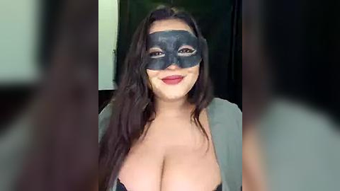 Media: Video of a smiling woman with long dark hair, wearing a black mask and revealing a low-cut gray top, exposing ample cleavage.