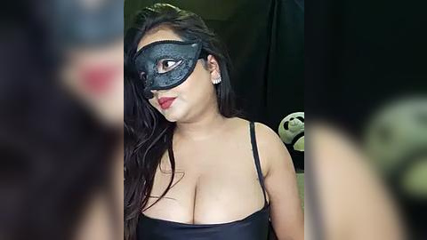 Media: Video of a woman with long black hair, wearing a black cat mask and a revealing black top, with a blurred background featuring a green and white striped toy.