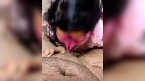 Media: Video of a woman with long black hair, wearing a pink dress, bending over a wooden table, with blurred background and unclear facial expression.