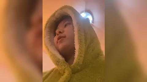 Media: A video of a young boy with fair skin, wearing a yellow bathrobe with a furry hood, looking upwards with a serene expression. The blurred background suggests a warm, possibly bathroom setting.