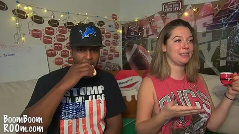 Media: A video of a young black man in a \"Bears\" t-shirt and cap eating a sandwich, and a young white woman in a \"Bucs\" t-shirt, both sitting on a couch in a room decorated with sports memorabilia and string lights.