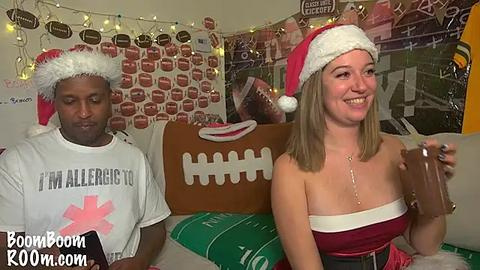 Media: Video of a black man in a white Santa hat and shirt, and a blonde woman in a red Santa hat and strapless dress, holding a dildo in a room decorated with football-themed posters.