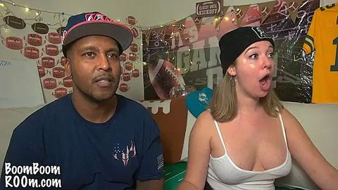 Media: Video of a Black man and a blonde woman in a living room, both wearing casual attire and laughing. Background features sports decor and a \"BoomBoomRoom.com\" watermark.