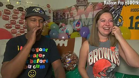 Media: Video of a smiling African-American man and a white woman, both wearing \"Browns\" jerseys, in a brightly decorated room with balloons and football-themed decorations.