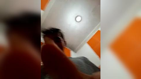 Media: A blurry video of a person with dark hair, possibly a man, in a room with orange and white walls and a circular light fixture.