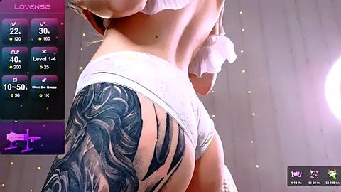 Media: Video of a woman in white underwear, showcasing a large black and gray tattoo sleeve on her left arm, standing against a wooden background with a glowing orb.