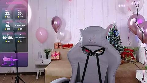 Media: Video of a cozy, festive living room with a gray gaming chair, white Christmas tree, pink balloons, and presents.