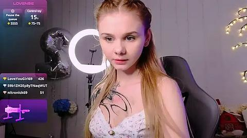 Media: A video of a young woman with long blonde hair, wearing a white lace bralette, seated in a chair, with a \"Love You Live\" stream overlay.