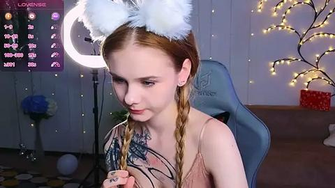 Media: Video of a pale-skinned, red-haired woman in a pink dress with white bunny ears, sitting in a chair with a crescent moon lamp and twinkling fairy lights in the background.