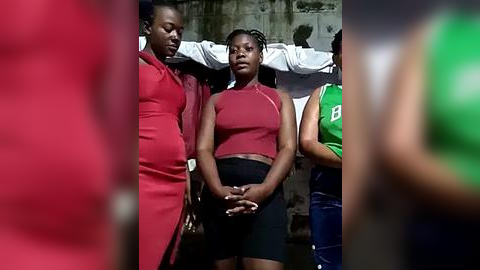 Media: Video of three African-American women in red, black, and green shirts, standing in a solemn, tight formation. They are dressed in casual, sporty attire, hands clasped together, and appear to be in a moment of solidarity or vigilance.