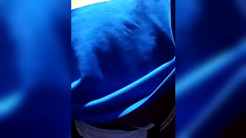 Media: A video featuring a close-up of a person's midsection, partially obscured by blue fabric, likely from a flowing garment. The skin appears smooth, and the background is blurred in shades of blue.