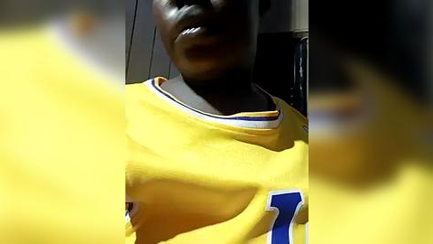 Media: Video of a dark-skinned person wearing a yellow basketball jersey with blue and white accents, partially blurred, likely in an indoor setting.