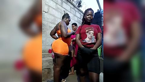 Media: Video of three Black women, one in an orange bikini, another in a red t-shirt and black shorts, and a third in a red dress, standing in a brick alley.