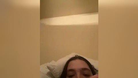 Media: A video captures a woman's face from the chest up, lying in a bathtub with white towels and beige walls. Her brown hair is wet, and she appears relaxed.