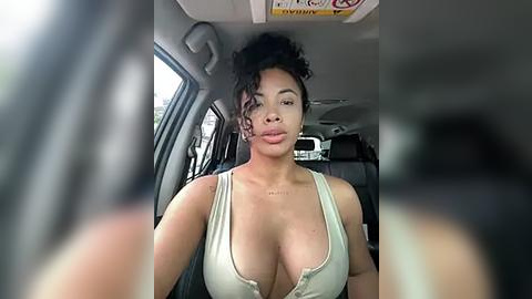 Media: A video of a light-skinned woman with curly hair, wearing a low-cut, white tank top, sitting in a car.