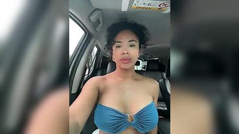 Media: Video of a young Black woman with natural curly hair, wearing a strapless blue bikini top, seated in the backseat of a car.