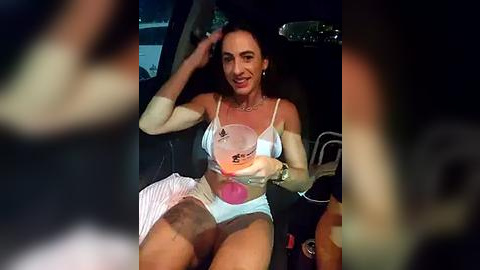 Media: A video of a woman with long dark hair and a medium build, wearing a white sports bra and shorts, holding a pink paddle inside a car.