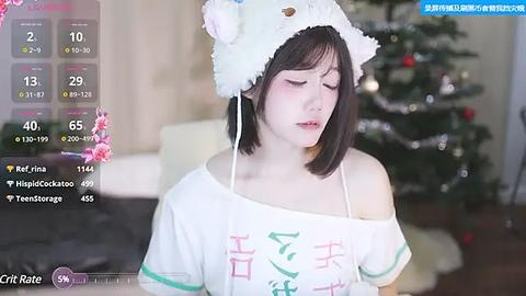 Media: Video of a young Asian woman with fair skin, wearing a white off-shoulder shirt, a cat hat, and a pink flower in her hair. She stands next to a decorated Christmas tree in a cozy room.