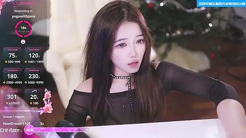 Media: A video of a young Asian woman with long black hair, fair skin, and a slender build, wearing a black off-shoulder top and choker necklace. She is in a modern indoor setting with a blurred Christmas tree background.