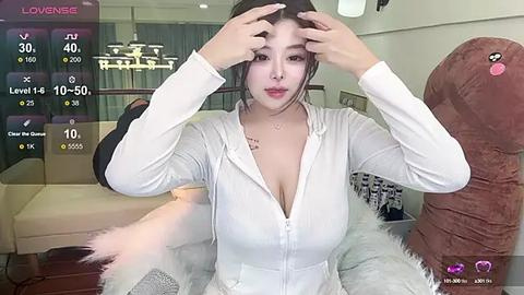 Media: Video of an East Asian woman with long black hair, wearing a white zip-up hoodie, adjusting her hair in a modern, well-lit living room.