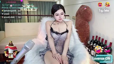 Media: Video of an Asian woman with light skin, dark hair, and medium breasts, wearing a revealing black lingerie dress, sitting on a fluffy white chair, surrounded by wine bottles, in a modern living room.