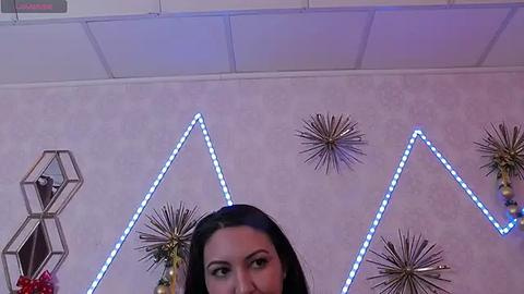 Media: Video of a woman with long black hair and light skin, partially visible, in a room with blue LED triangle lights, star ornaments, and a Christmas tree.