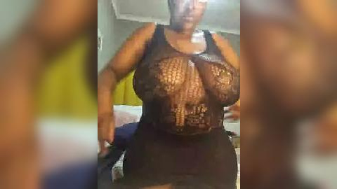 Media: A blurry video shows a plus-sized Black woman with large breasts in a sheer black mesh top, revealing her nipples, and a black skirt, standing in a dimly lit bedroom.