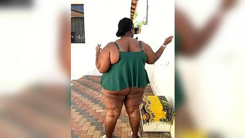 Media: Video of a plus-size woman in a green tank top, standing on a sunlit patio, with a colorful rug in the background.