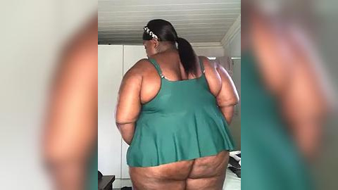 Media: Video of a plus-sized Black woman in a green tank top, viewed from behind, showing her large, bare buttocks. The background is a simple bedroom with white walls and a closet.