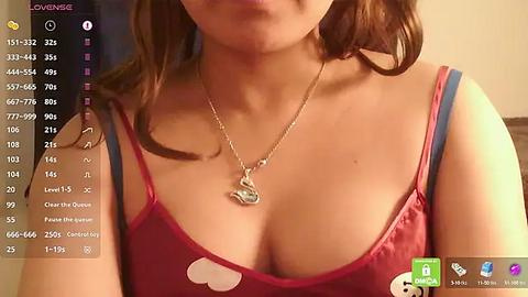 Media: Video of a light-skinned woman with shoulder-length brown hair, wearing a red tank top with a heart-shaped cutout, showcasing her ample cleavage. The background is blurred, suggesting an indoor setting.