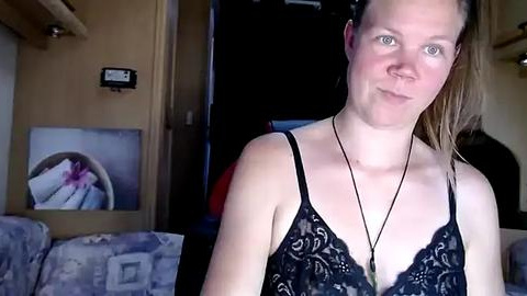 Media: Video of a blonde woman with fair skin, wearing a black lace bra, standing indoors in a dimly lit room. Background features a closed door, a wooden panel, and a framed painting.