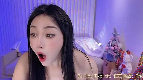 Media: A video of an Asian woman with long black hair, fair skin, and full makeup, wearing a sultry expression and nothing but her mouth. She is indoors, in a bedroom with a Christmas tree and a bed.