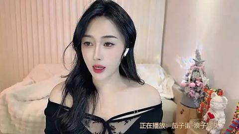 Media: Video of an Asian woman with long black hair, wearing a black lace top, white earbuds, in a cozy bedroom with a lit Christmas tree, white bed, and festive decorations.