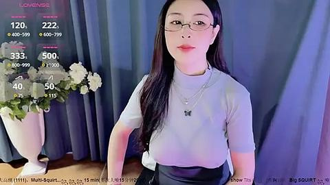 Media: A video of an Asian woman with long black hair, wearing glasses and a white turtleneck, standing against a blue curtain background, holding a phone.