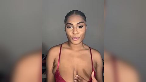 Media: A video of a Black woman with dark skin, wearing a red lace bra, standing against a plain gray background. She has a slender build and medium-sized breasts.