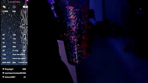 Media: A video of a black person, possibly male, wearing a colorful, abstract patterned shirt, standing in a dimly lit room with blue lighting. The background is out of focus, and the image has a grainy texture.