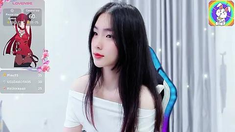 Media: A video of an Asian woman with long black hair and fair skin, wearing a white off-shoulder top, in a gaming chair, with a virtual character overlay.