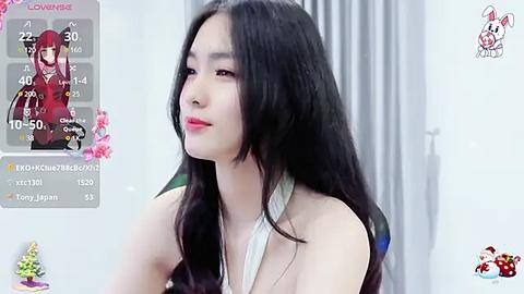 Media: Video of a fair-skinned, long-haired Asian woman with red lipstick, wearing a sleeveless white top, looking pensive. Background shows a white room with a flower arrangement.