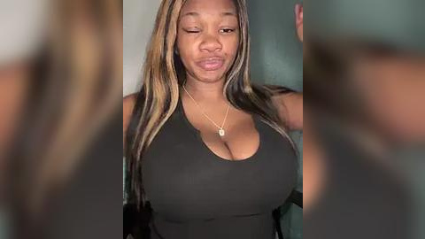 Media: Video of a young Black woman with long, straightened hair, wearing a black tank top that accentuates her large breasts. She has a neutral facial expression, and a blurred background.