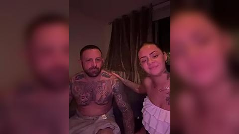 Media: A blurry video of a tattooed man and a woman with a ponytail in a dimly lit room, wearing revealing clothing.