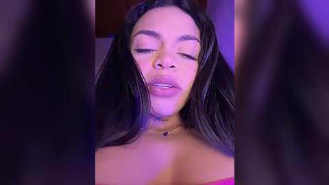 Media: Video of a light-skinned Black woman with long, straight black hair, wearing a pink top, eyes closed, smiling softly, against a purple-lit background.