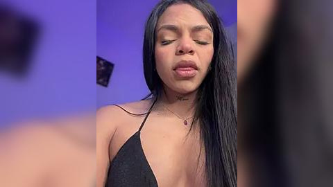 Media: Video of a young, attractive Black woman with long, straight black hair, wearing a black halter top, with a small tattoo on her neck. She has a closed-mouth, serene expression, set against a purple-hued background.