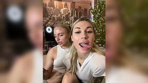 Media: Video of two young women with blonde hair, wearing white tops, in a festive room with Christmas decorations and a large, blurred figure in the background.