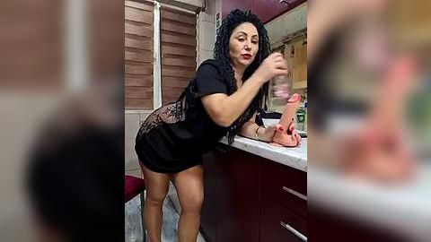 Media: A video of a curvy, dark-haired woman in a black lace lingerie set, applying lipstick in a kitchen with red cabinets and a countertop.